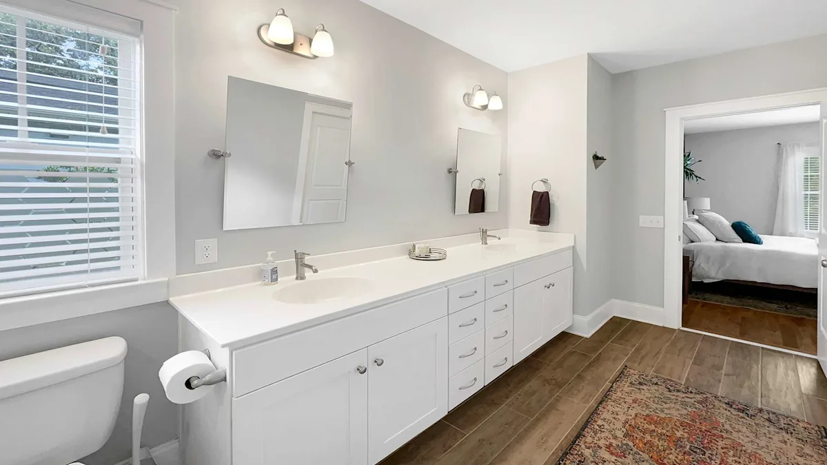A modern bathroom with a double vanity, toilet, and a doorway to a bedroom