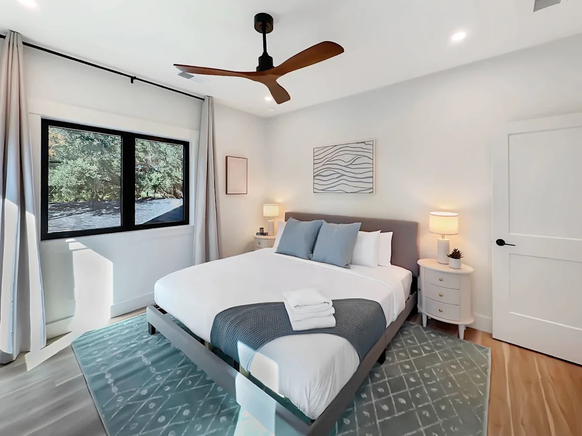 A wide view of a bedroom with a large bed, two nightstands, a window, and a ceiling fan.