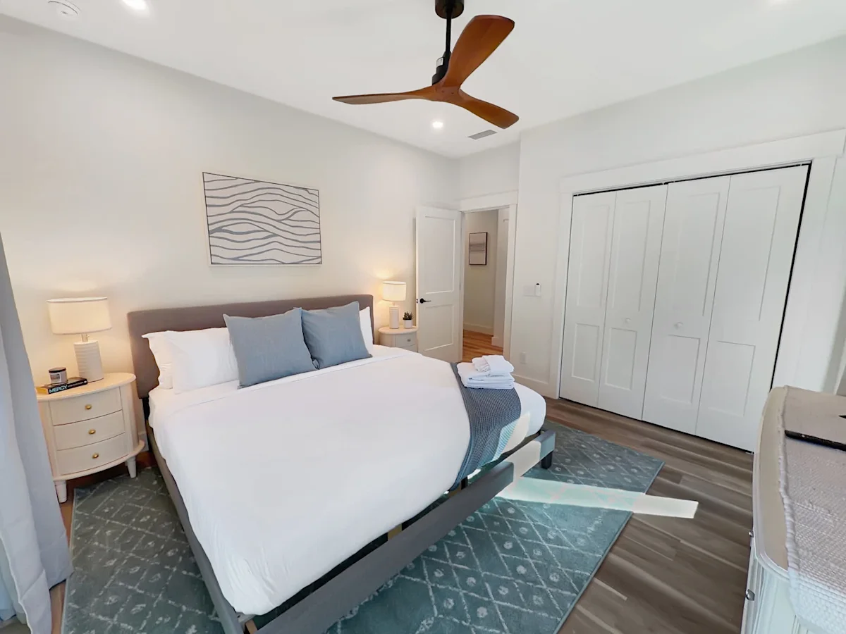 A wide-angle view of a bedroom with a large bed, nightstands, and a closet.