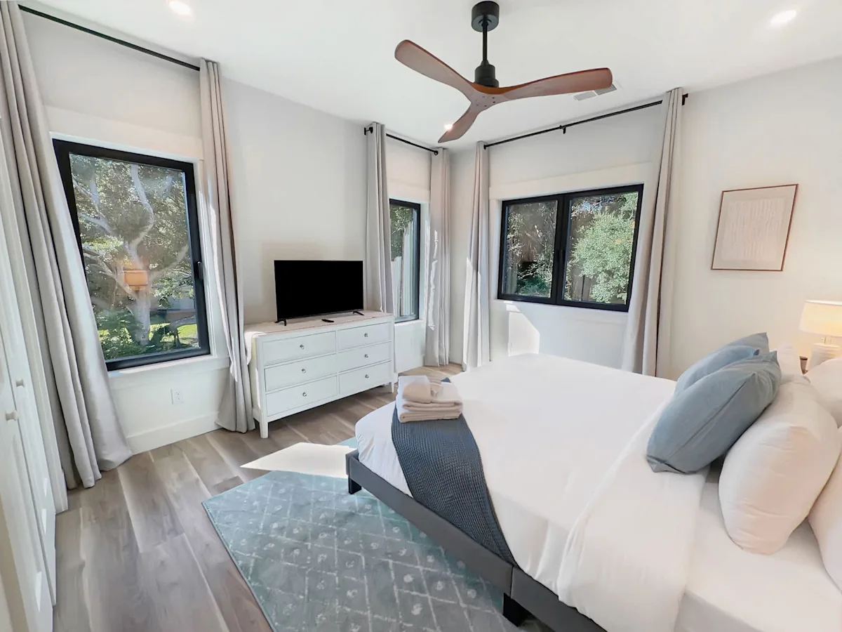 A white bedroom with a large bed, dresser, and TV