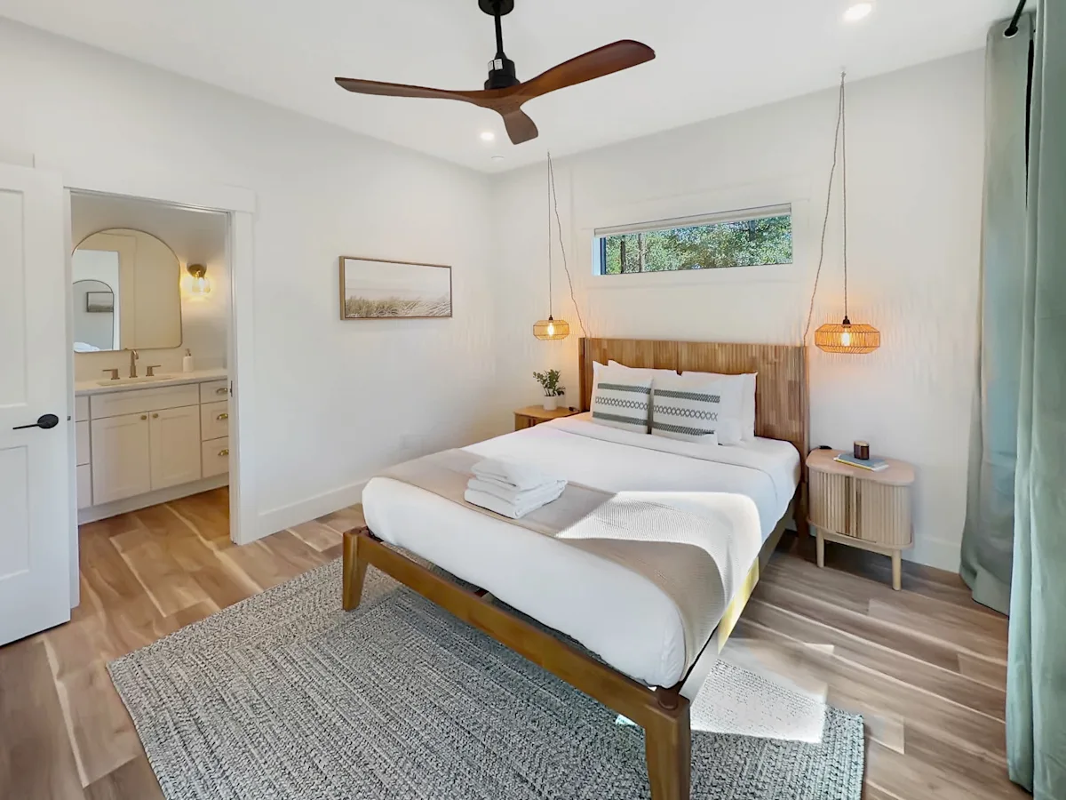 A bright and airy guest room with a large bed, wooden floor, and pendant lights.