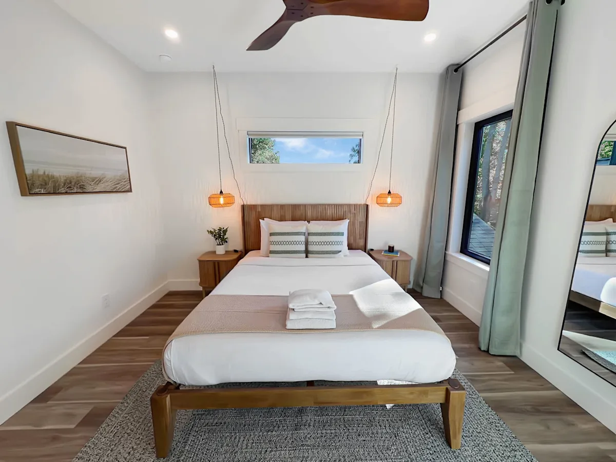 A neatly made bed in a small room with white walls, wooden floor, and a ceiling fan.