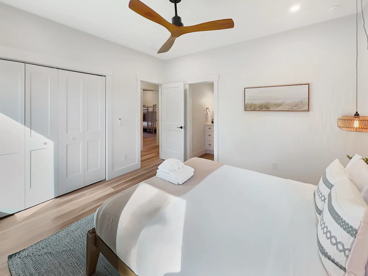 A neatly arranged bedroom with a large bed, ceiling fan, and doorway to another room