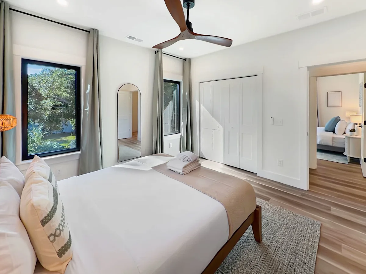 A wide view of a bedroom with a bed, window, ceiling fan, and closet.
