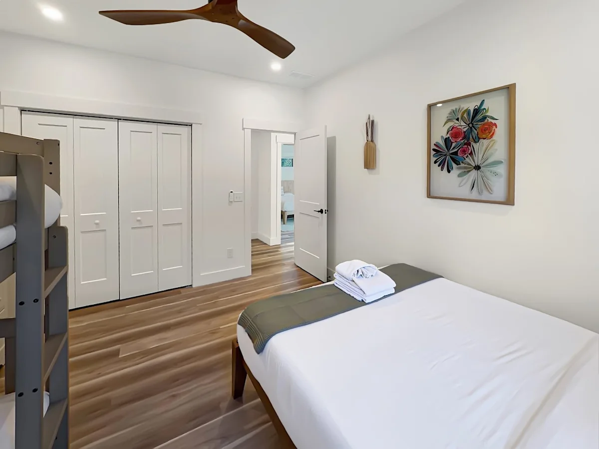 A wide view of a room with a bunk bed, a single bed, and a doorway leading to another room.
