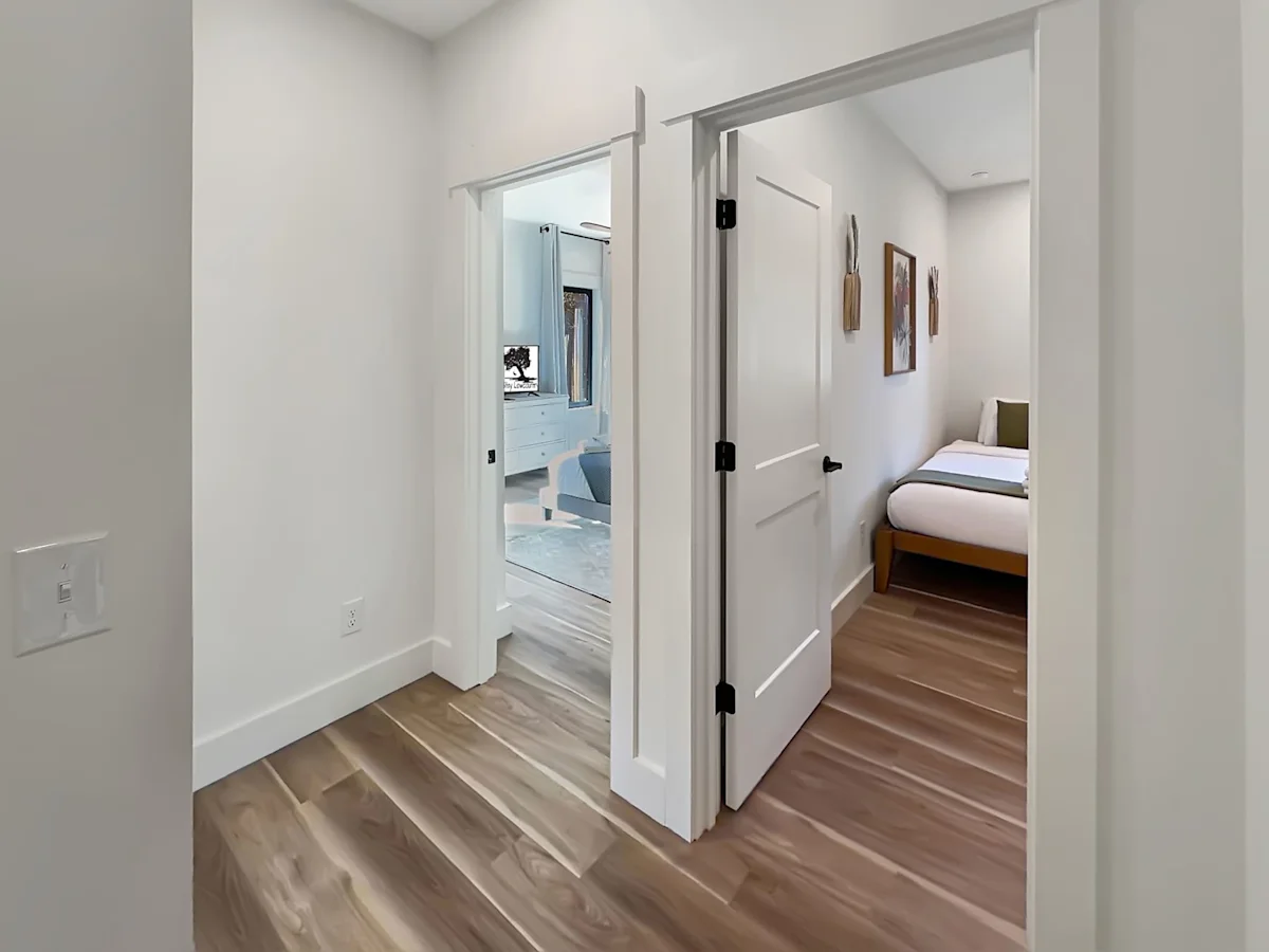 A wide view of a room with white walls and wooden floors, showing an open doorway into a bedroom