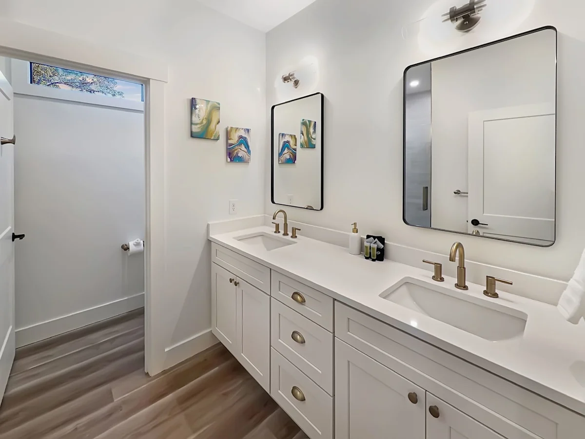 A clean and modern bathroom with a double vanity, two large mirrors, and artwork on the wall.