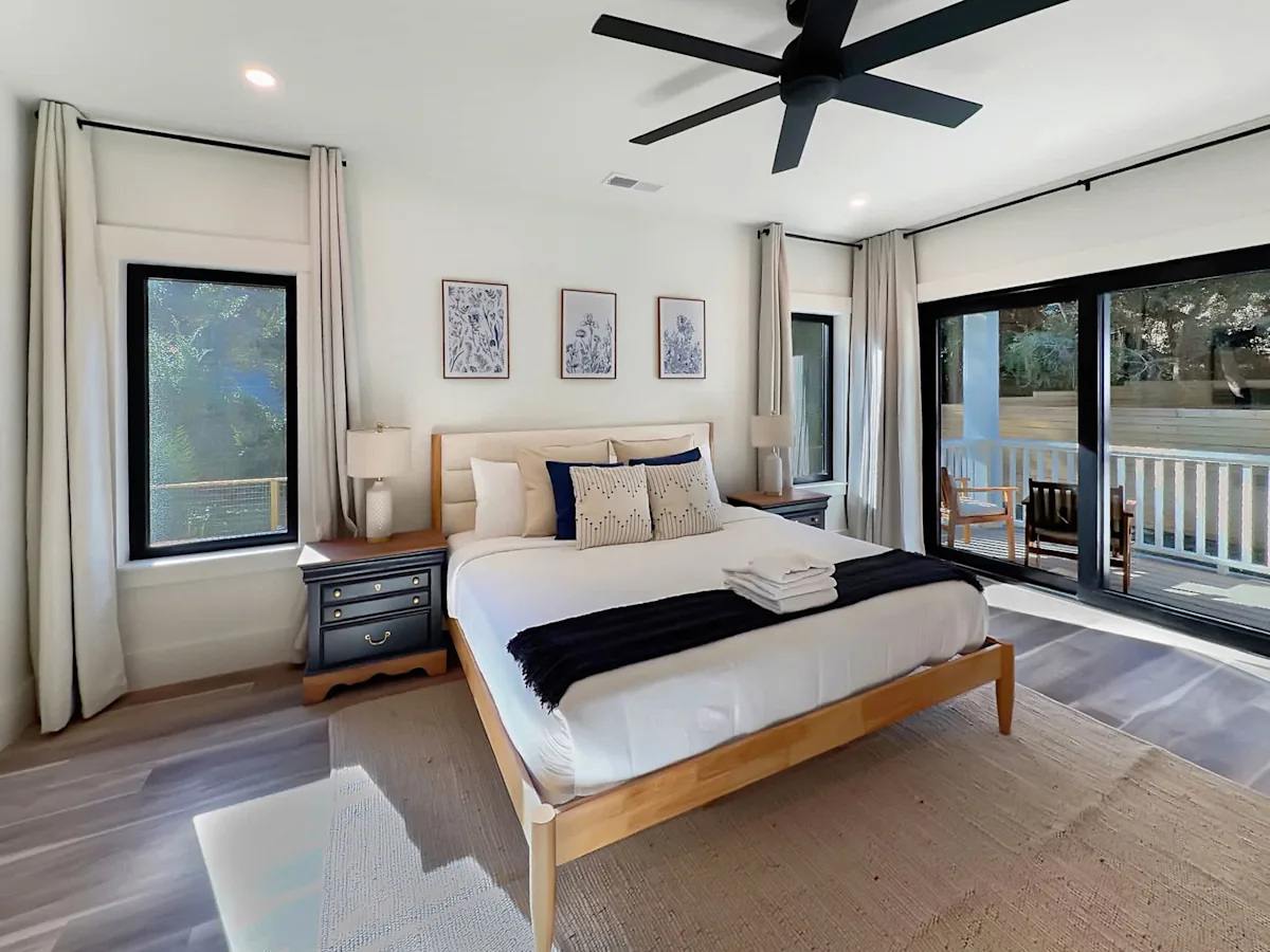 A wide view of a bedroom with a large bed, two nightstands, a window, and a sliding door leading to a balcony.