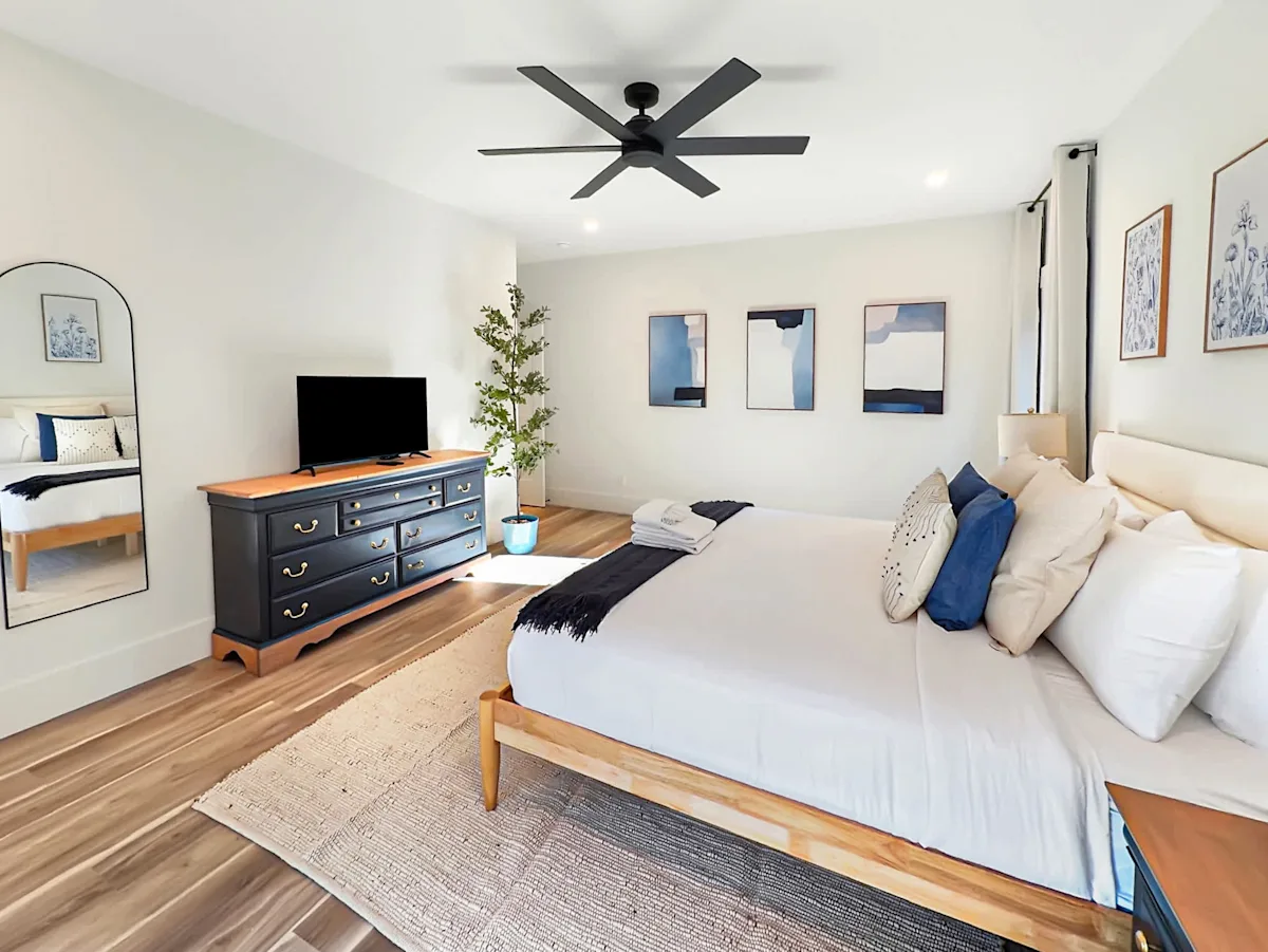 A wide-angle view of a bedroom with a large bed, dresser, and TV.