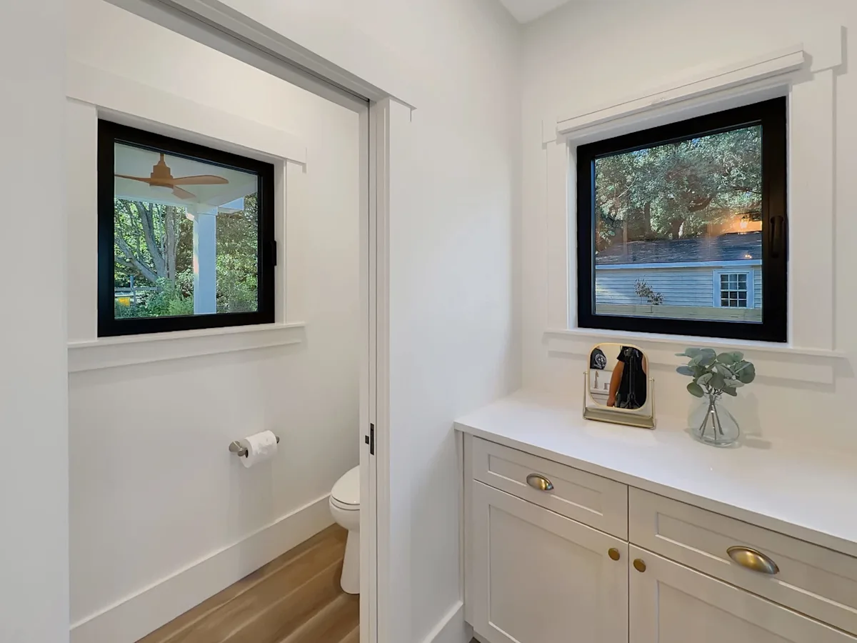 a white bathroom with a window above the toilet and another above a cabinet