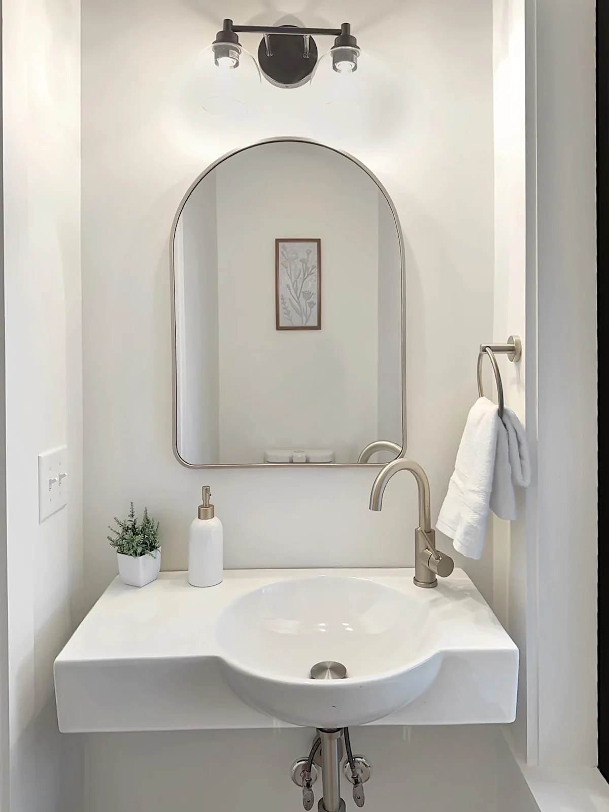 A clean and modern bathroom sink area with a large mirror, a white towel, and a small plant.