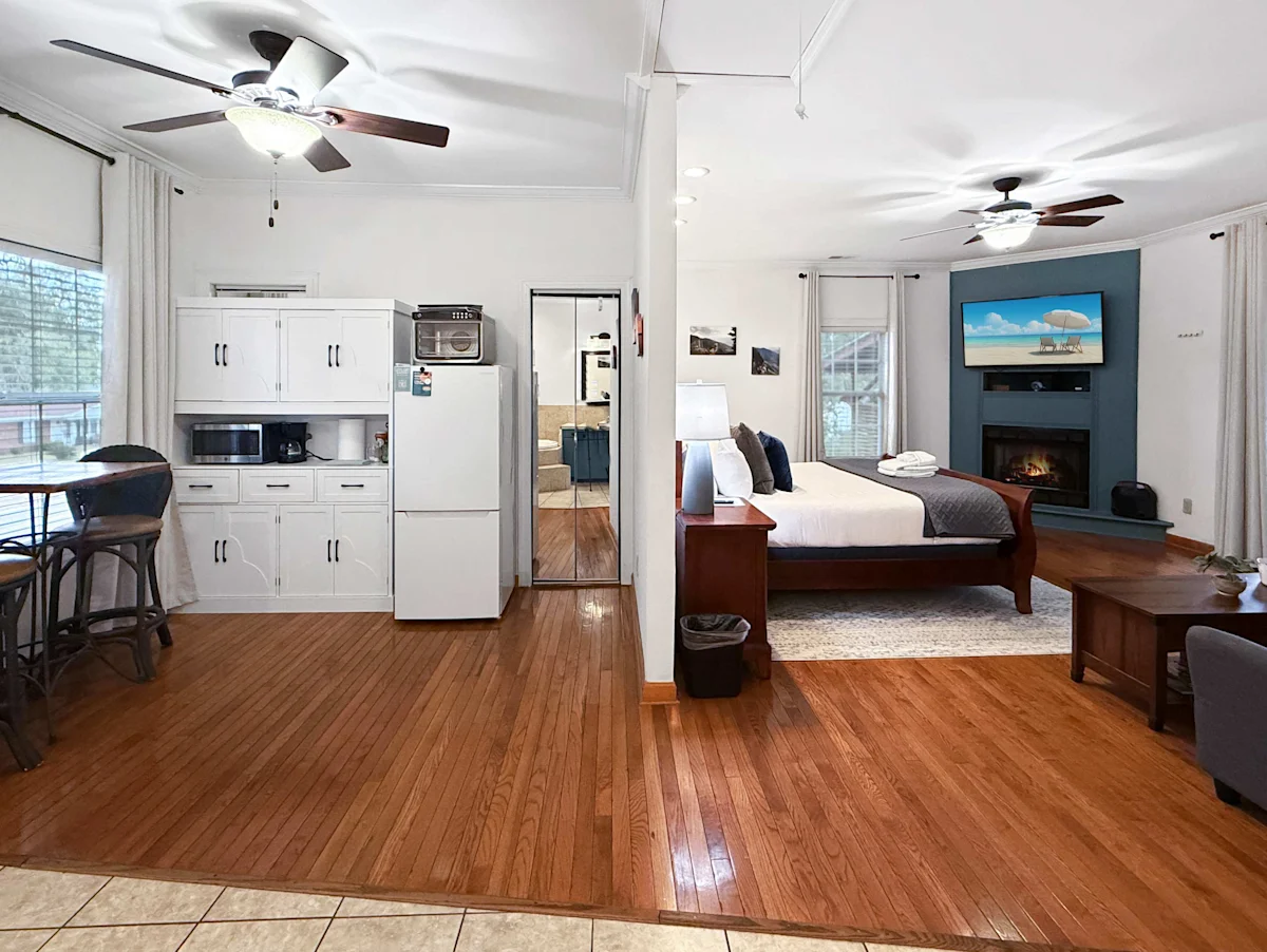 A wide view of a suite with a kitchenette, bed, fireplace, and TV.