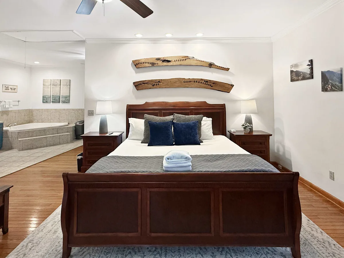 A large hotel room with a king-size bed, two nightstands with lamps, and a soaking tub in the background.