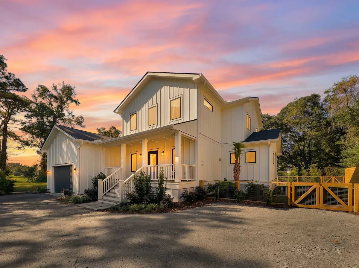 A two-story white house with a porch and a garage under a colorful sunset sky.