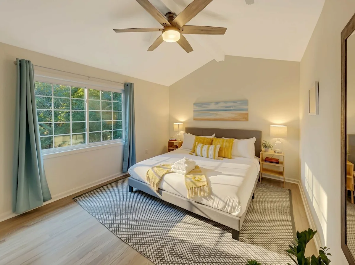 A bright and airy bedroom with a large bed, two nightstands, and a window with blue curtains.