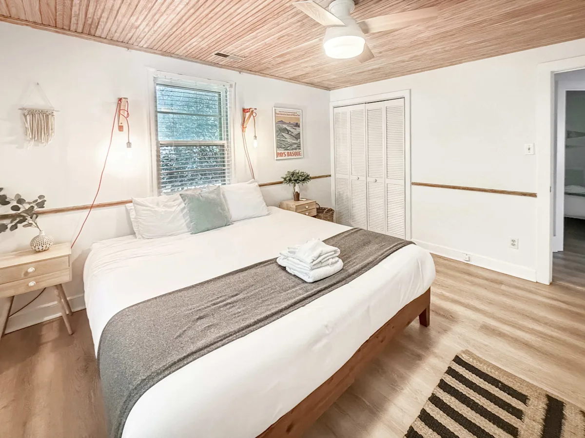 A wide view of a guest room with a bed, nightstand, closet, and window