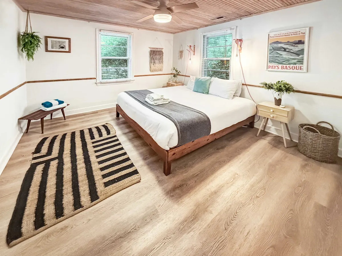 A wide-angle view of a bedroom with a large bed, nightstand, and rug.