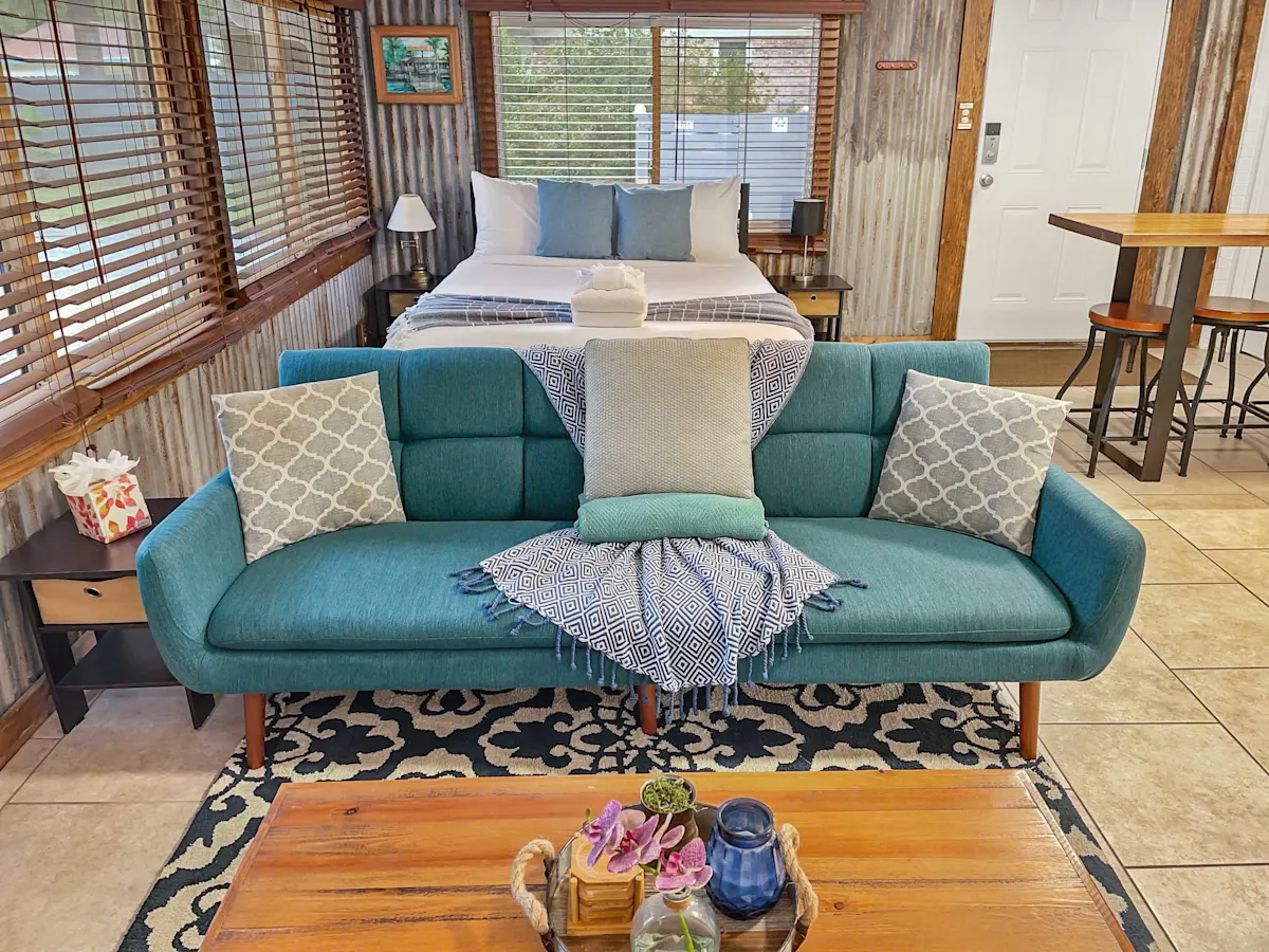 A cozy room with a teal couch, wooden coffee table, and a bed in the background.