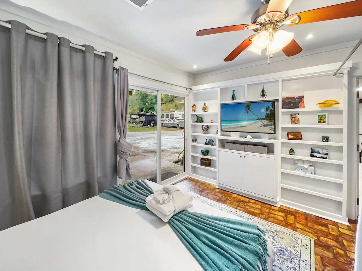 A hotel room with a bed, TV, and bookshelf