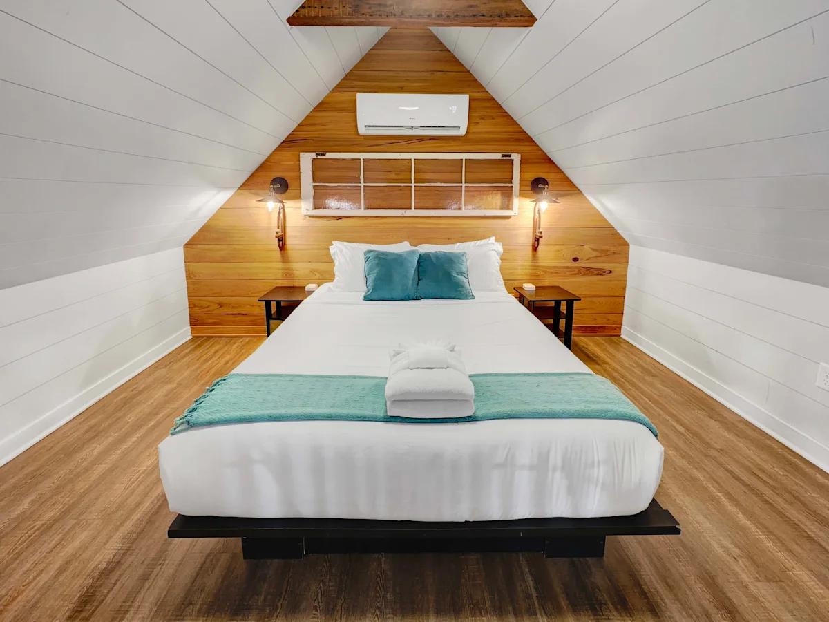 A neatly made bed in a cozy attic room with wood paneling and a vaulted ceiling.