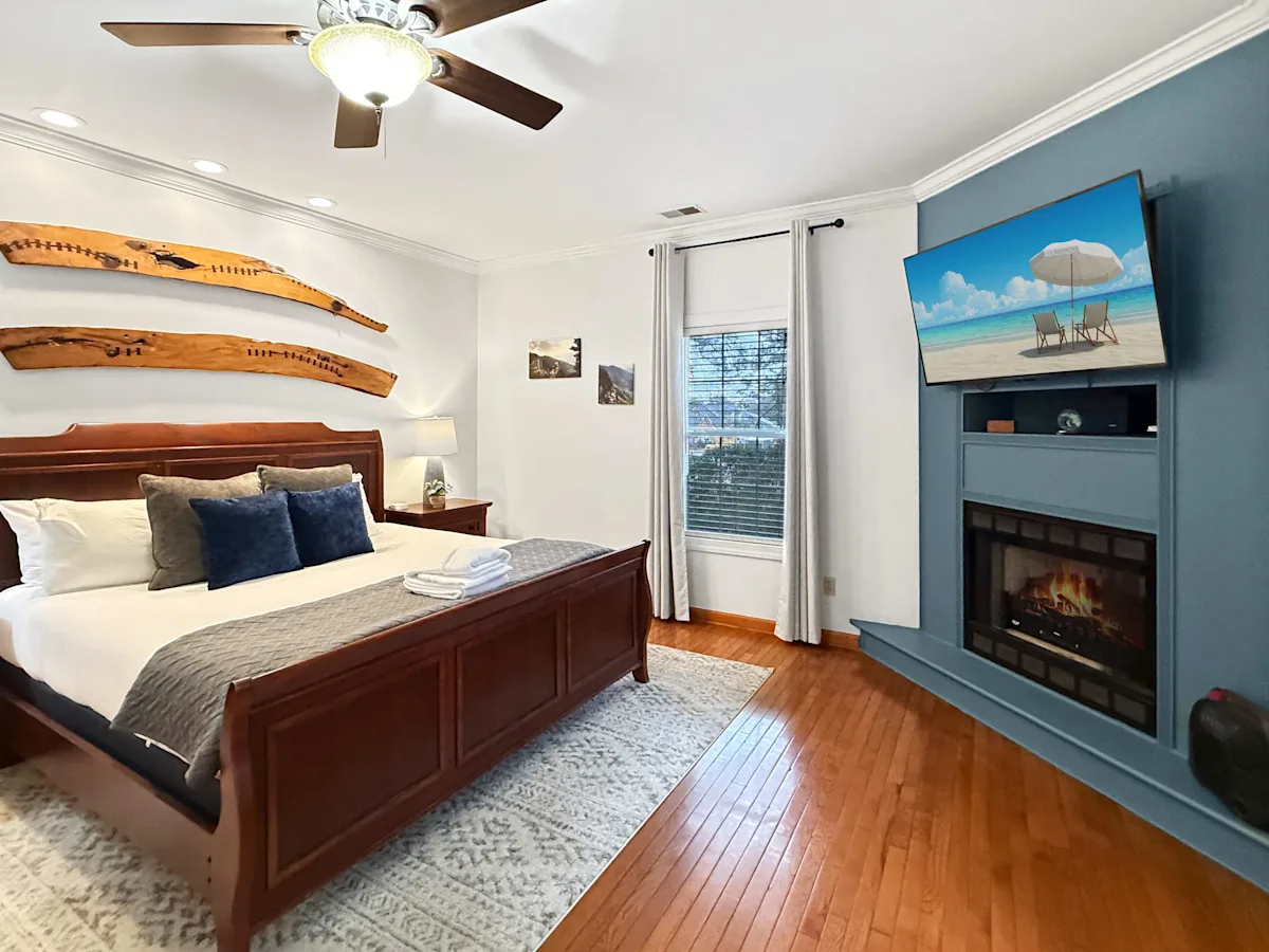 A wide-angle view of a bedroom with a bed, fireplace, TV, and ceiling fan.