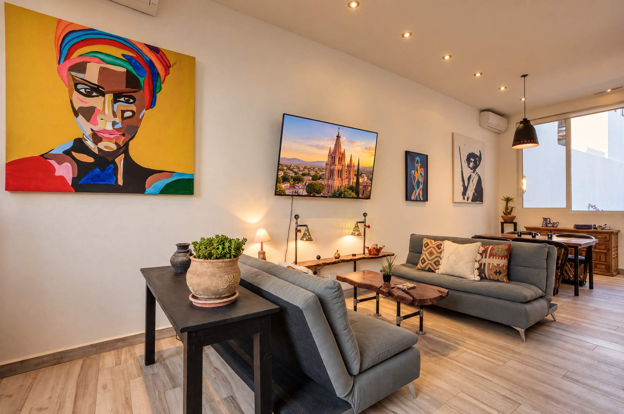 Sala con sofás grises, retrato de arte pop colorido y obras de arte local en muros luminosos