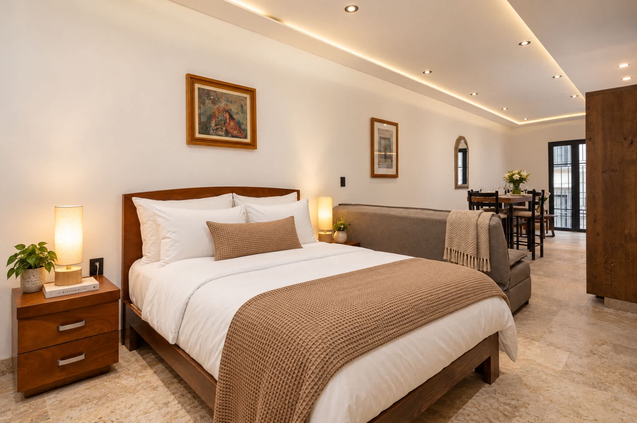 Recámara con cama queen, buró de madera y iluminación cálida con vista al área de comedor