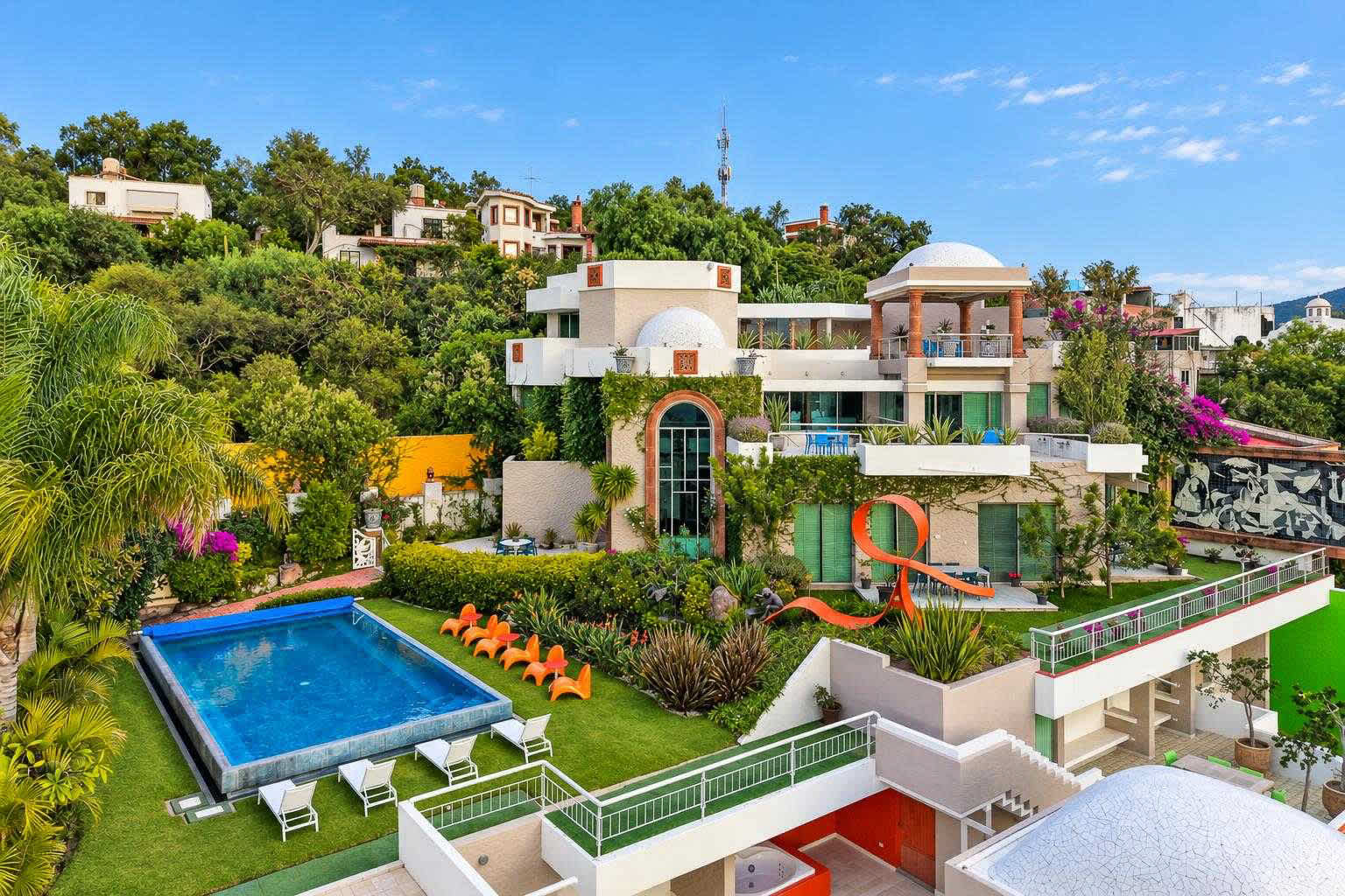 Colorful multi-level home with swimming pool, lounge chairs, and manicured gardens