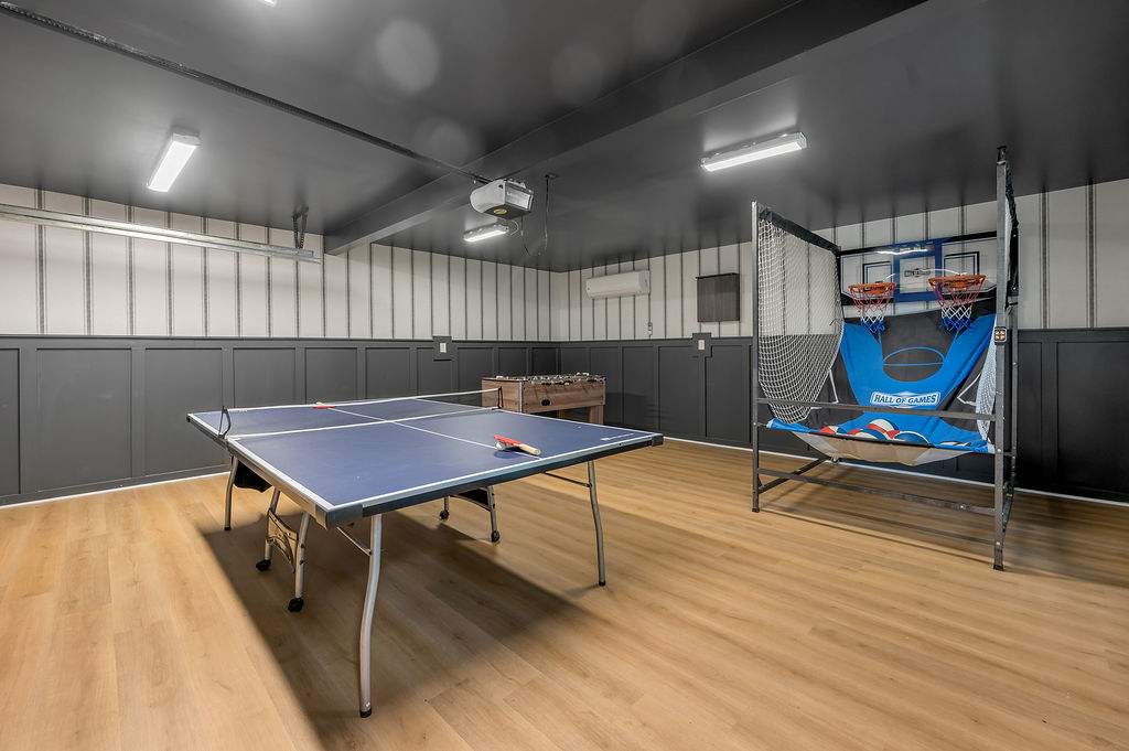 Head into the garage-turned-arcade for the whole lineup — foosball, ping pong, a wall-mounted basketball arcade, and a projector waiting on movie night with the whole crew.
