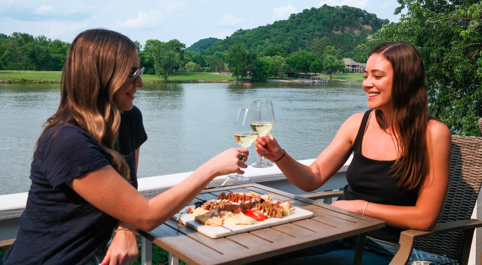 Two friends toasting on the riverside deck of a Venturebnb home near Nashville