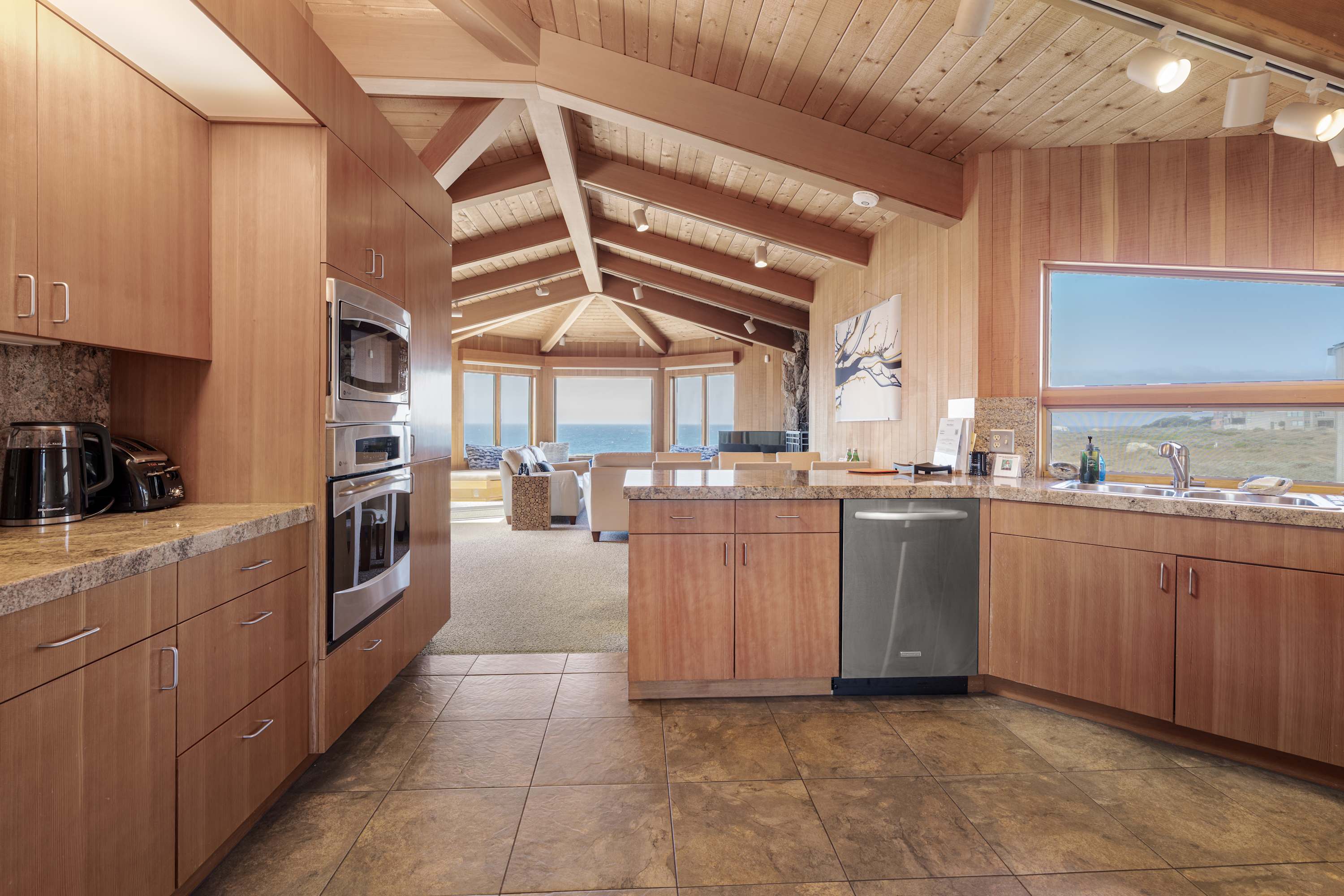 Cook on granite counters under skylights and track lighting, the living room and ocean glowing at the far end of the kitchen.