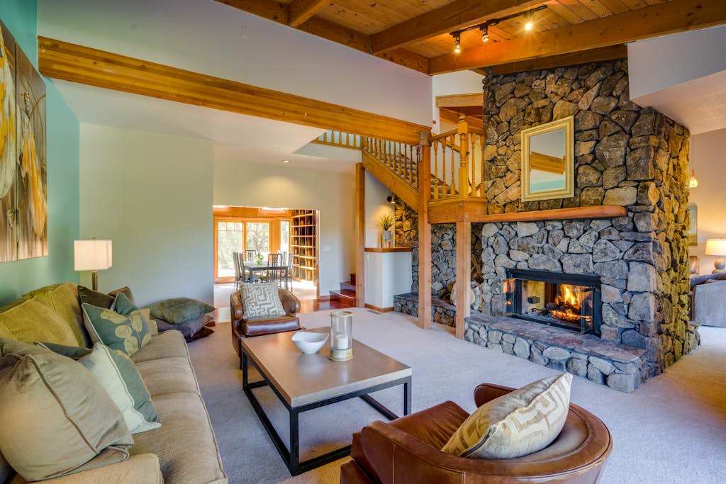 Gather your group across plush seating beneath soaring cathedral ceilings — the floor-to-ceiling stone fireplace anchors this lodge-like great room.