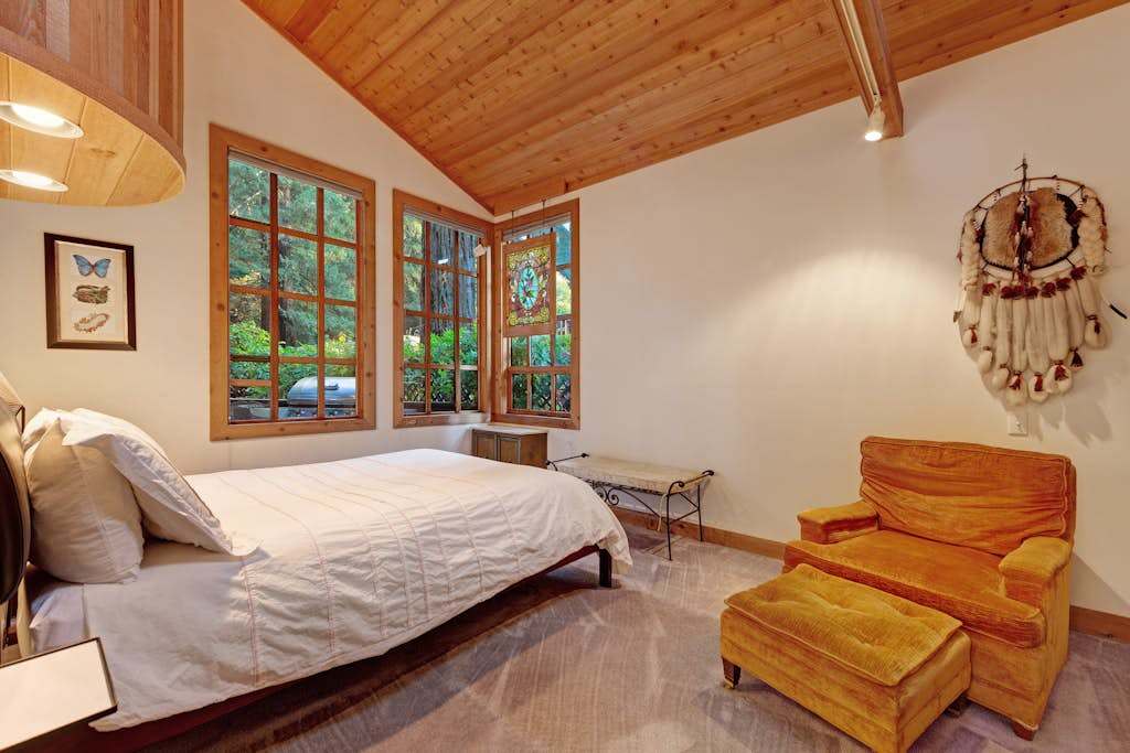 Rest peacefully in your serene bedroom with treetop views through wood-framed windows and a plush reading chair.