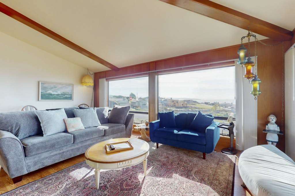 Sink into plush sofas and gaze out at Bodega Bay through panoramic windows in your sun-drenched coastal living room with vaulted beam ceilings