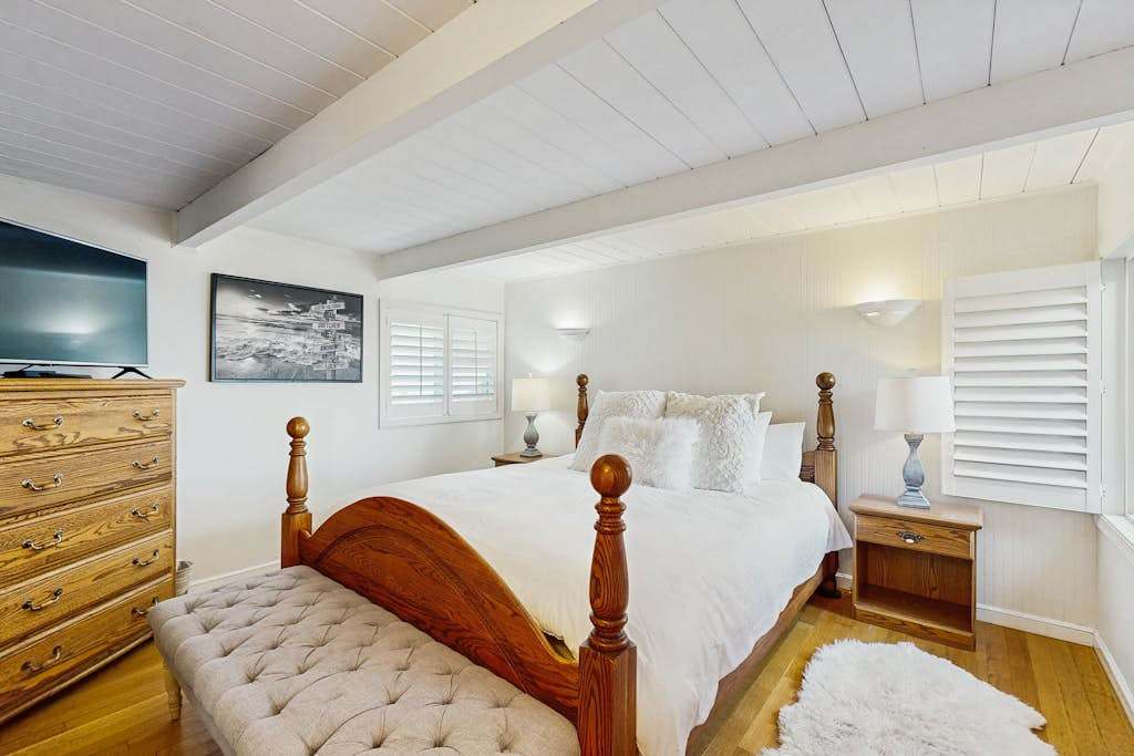 Rest in your serene primary bedroom with elegant four-poster bed, flat-screen TV, and hardwood floors