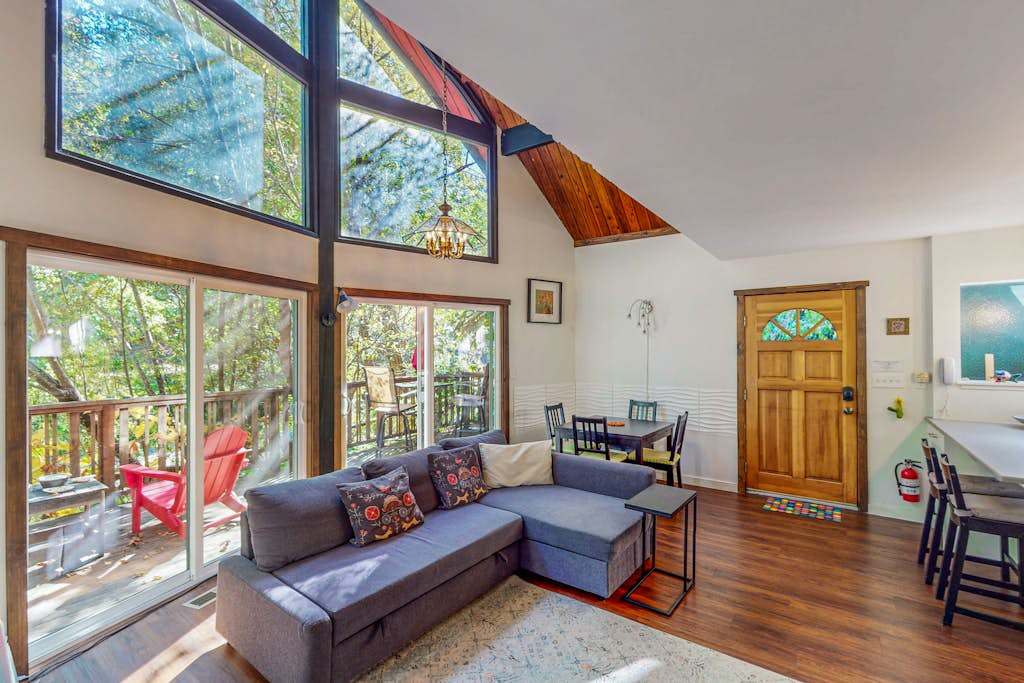 Sunlight floods your vaulted A-frame living room through soaring windows — sink into the sectional and watch redwood canopy sway just beyond the deck.