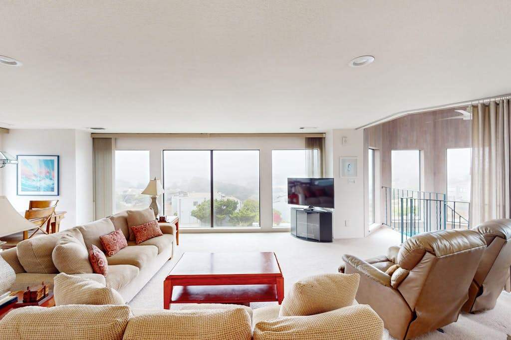 Sink into plush seating in your sunlit living room where panoramic Bodega Bay views stretch beyond floor-to-ceiling windows and a private balcony