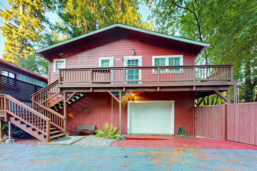 Welcome to your classic redwood-country retreat — Villa Eileen's warm red exterior, private garage, and upper deck tucked beneath towering trees.