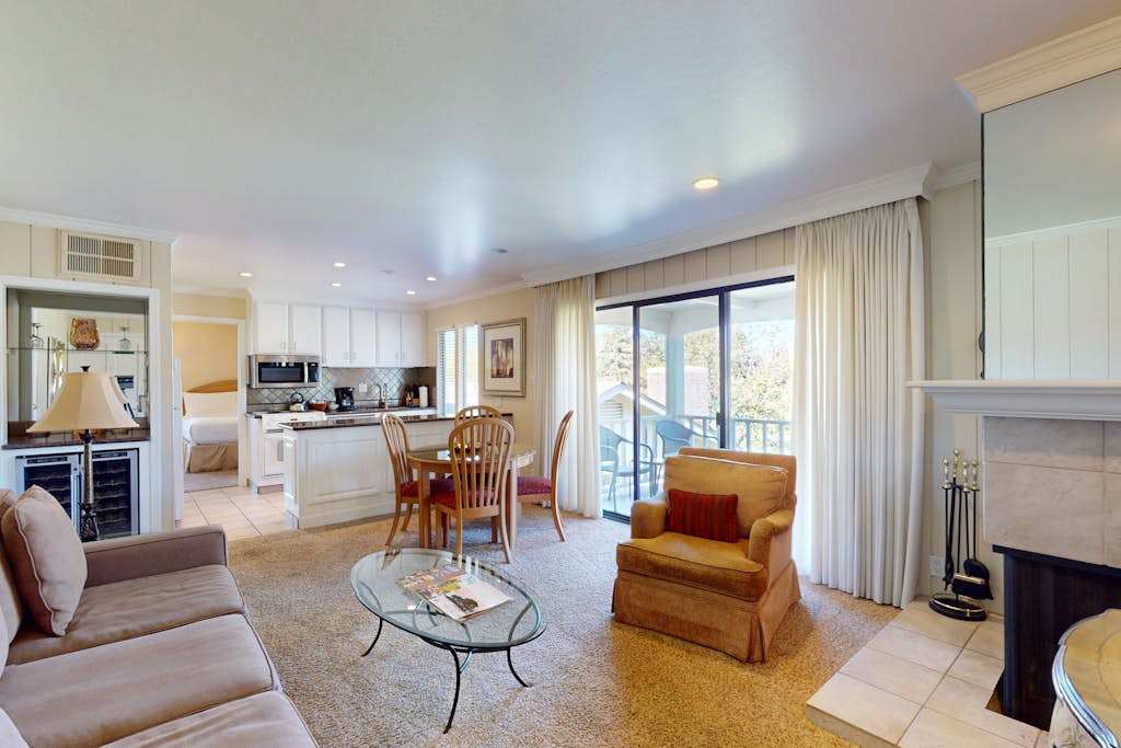 Step into your sunlit Napa Valley retreat — an open-concept living space with kitchenette, cozy seating, and sliding glass doors framing your private balcony view.
