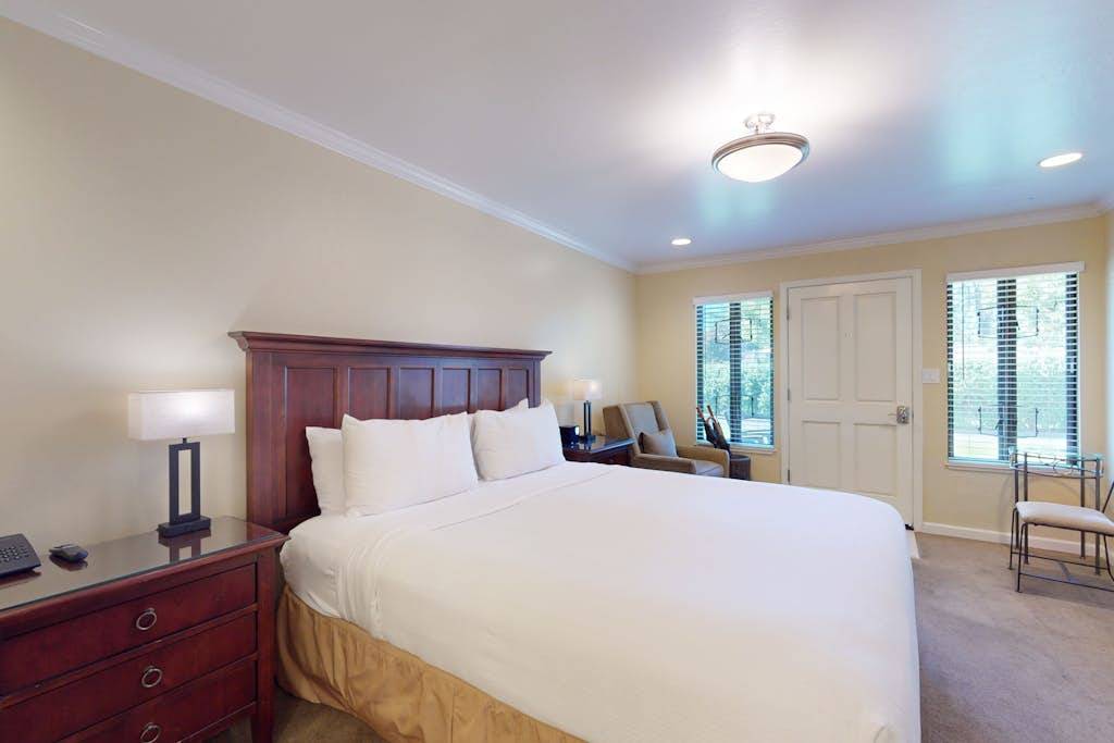Settle into your plush king bed after a day exploring Napa Valley wineries — crisp white linens, elegant dark-wood furnishings, and soft lighting set the tone for a restful retreat.