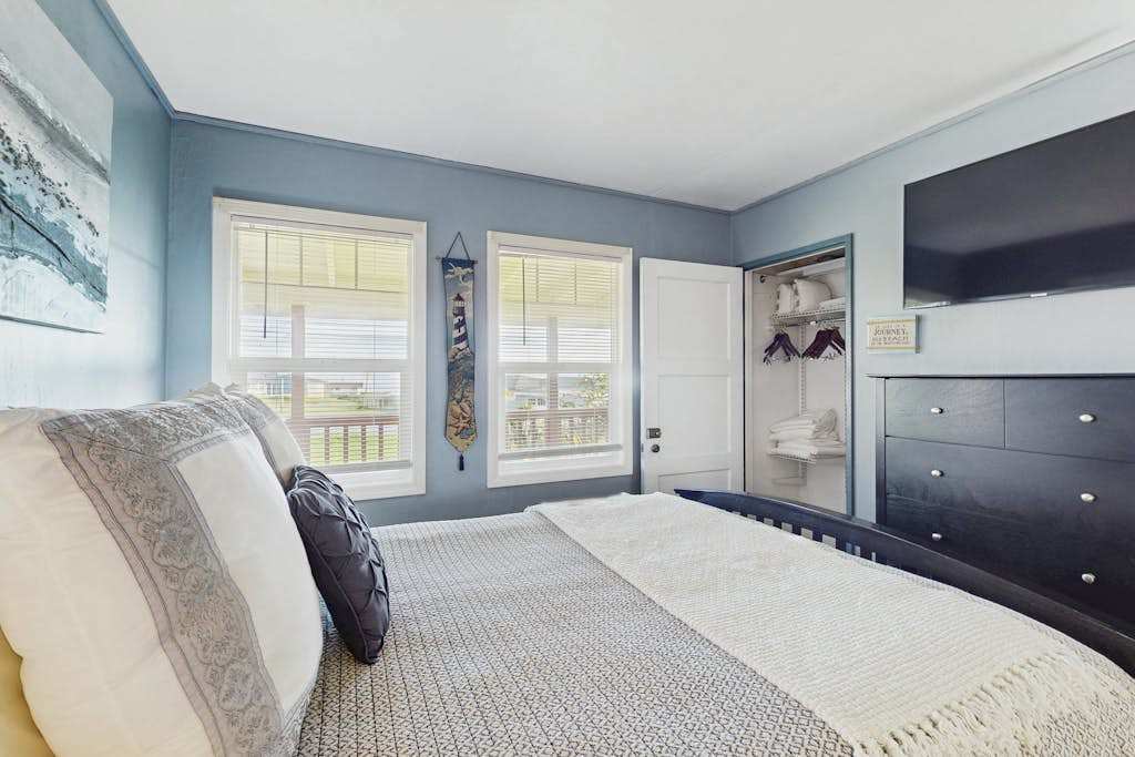 Step from your seaside-blue bedroom directly onto the deck through a private door — the wall-mounted TV and dark-wood dresser keep your retreat both stylish and functional.