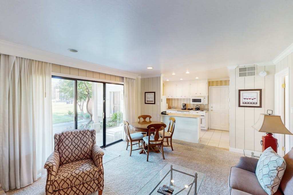 Settle into your open-concept living space with golf course views streaming through floor-to-ceiling sliders — kitchen, dining, and lounge all in one bright room.
