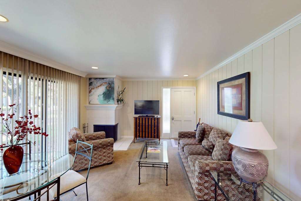 Relax in your stylishly appointed Napa condo living room featuring comfortable seating for four, a large flat-screen TV, and natural light streaming through the glass patio door.