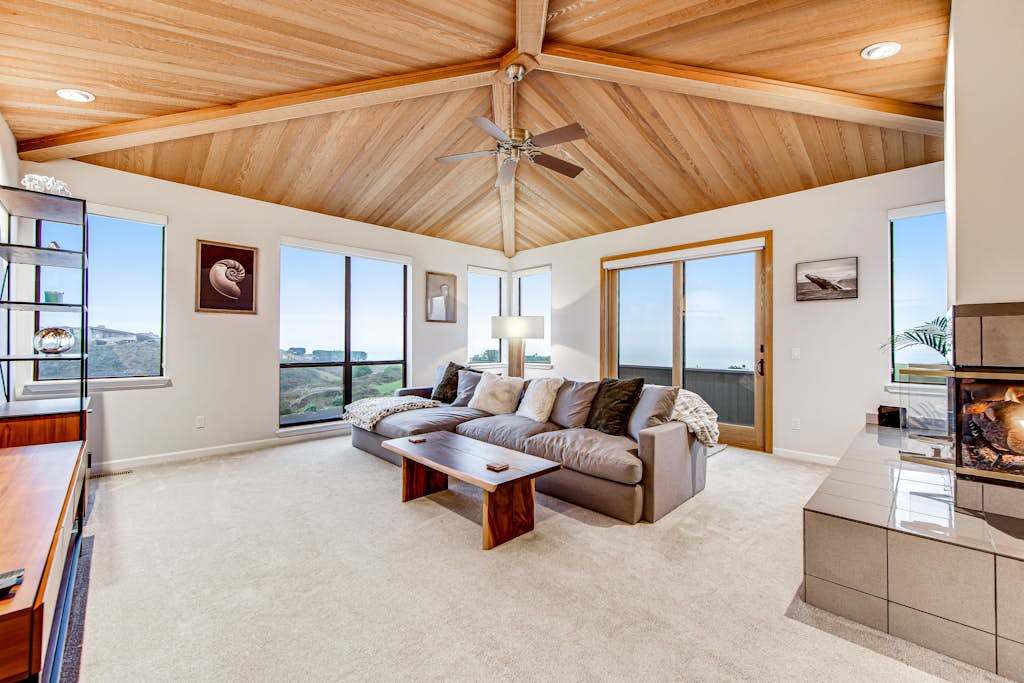 Gather beneath soaring vaulted wood ceilings in your main living room — panoramic windows fill the space with golden coastal light all day long