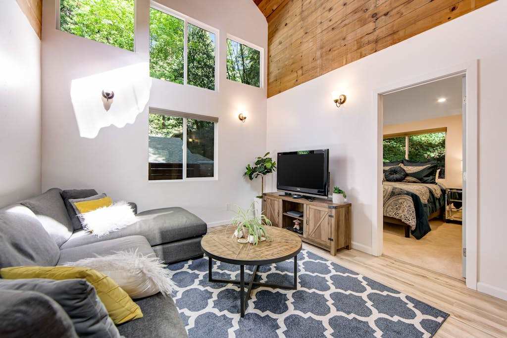 Settle into your sun-drenched living room with soaring wood-paneled ceilings, oversized windows framing the redwood canopy, and a cozy sectional for movie nights.