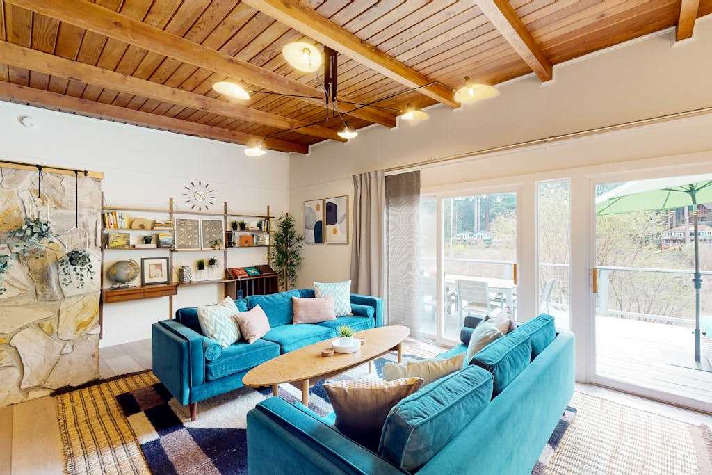 Settle into your sun-drenched living room where warm wood-beam ceilings and vibrant teal sofas invite you to relax after a day exploring Russian River wine country.