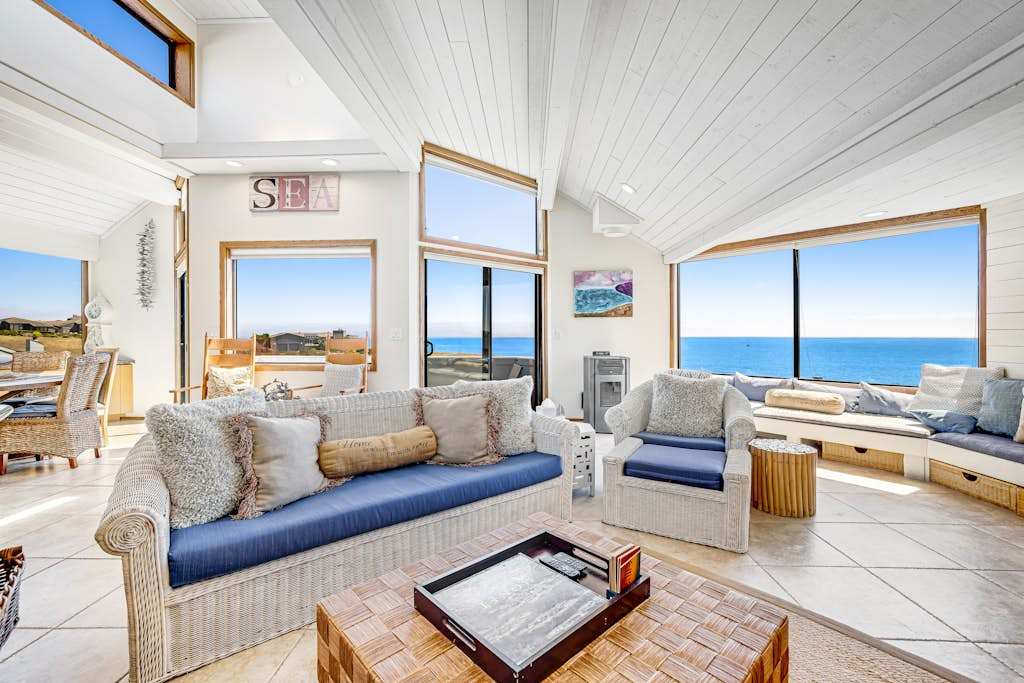 Sink into coastal comfort in your sun-drenched living room where panoramic Bodega Bay views stretch across the horizon through floor-to-ceiling windows