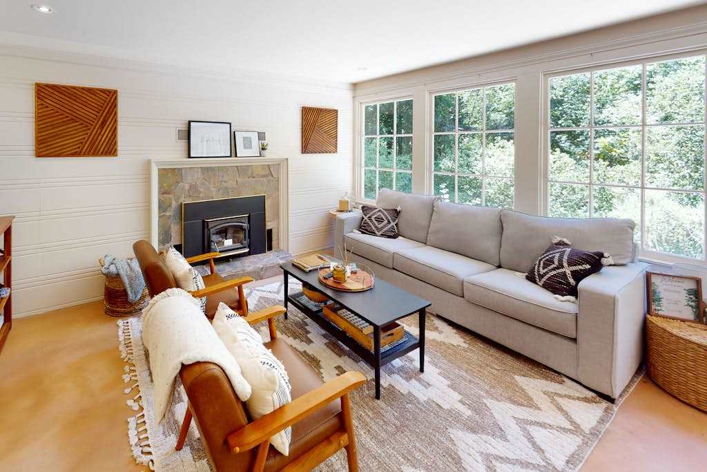 Sink into your sun-drenched living room where a stone fireplace, plush seating, and walls of windows frame the surrounding redwood canopy — your Guerneville escape starts here.