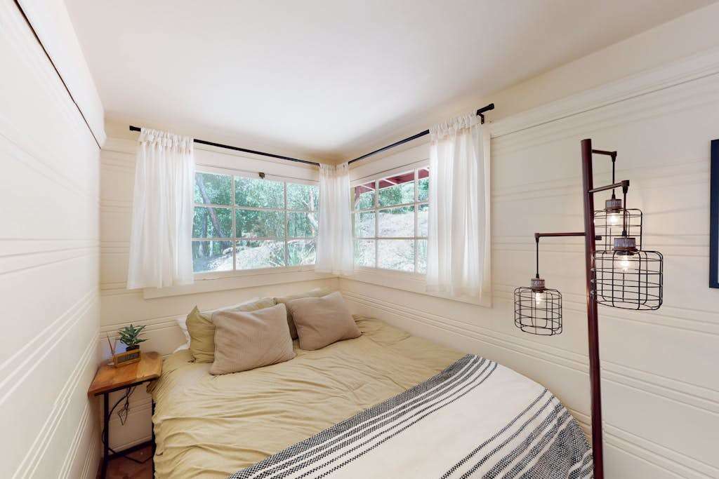 Drift off in your cozy queen bedroom wrapped in shiplap and soft linens — industrial cage pendant lights and corner windows bring rustic Guerneville charm to every detail.