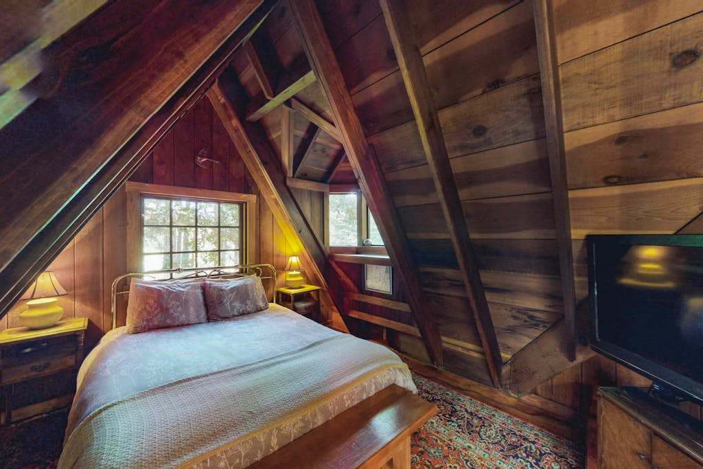 Drift off in your enchanting loft bedroom — a plush queen bed, peaked redwood A-frame ceiling, and treetop views through the dormer create your Cazadero dreamscape.